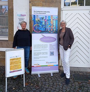 2 Frauen stehen vor einem Gebäude und schauen in die Kamera