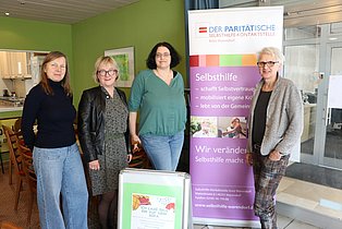 4 Menschen stehen in einem Raum und schauen in die Kamera