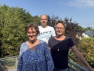 2 Frauen und 1 Mann stehen zusammen und schauen in die Kamera