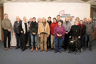 Eine Gruppe von Menschen steht in einer Reihe und schaut nach vorne in die Kamera